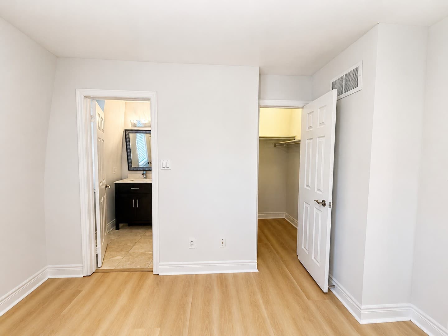 View from empty primary bedroom into ensuite bathroom and walk-in closet
